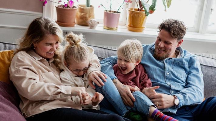Familie med mor, far og to barn sitter i sofa 
