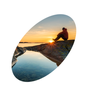 Illustrasjonsfoto av mann som sitter på berget ved vannkanten i solnedgangen