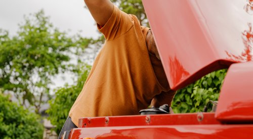 Illustrasjonsfoto av mann som ser under panseret på en rød bil.