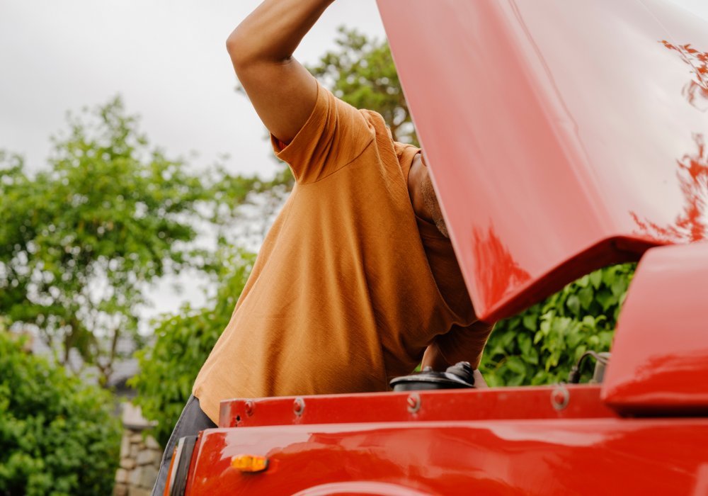 Illustrasjonsfoto av mann som ser under panseret på en rød bil.