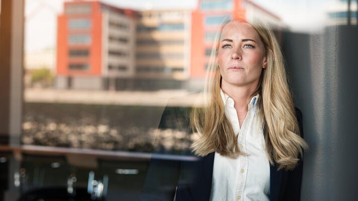 Dame i hvit skjorte og blazer som ser ut av et vindu.