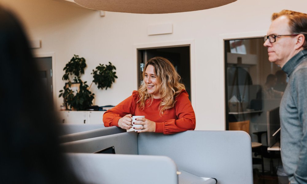Illustrasjonsfoto: Dame med kaffekopp prater med kolleger i åpent kontorlandskap 