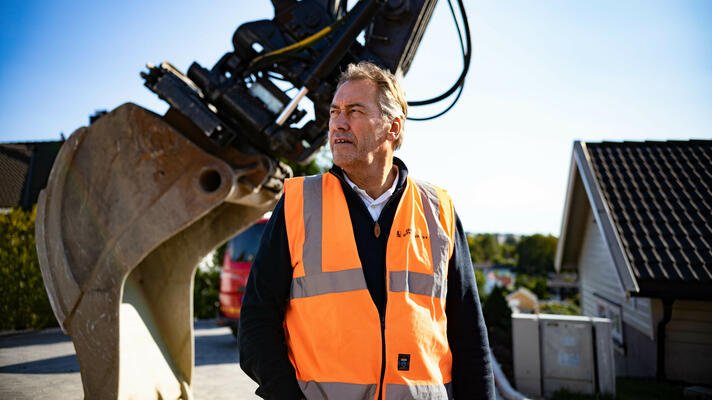Terje Andersen, administrerende direktør i Råde Graveservice, ute på en byggeplass med gravemaskin i bakgrunnen.