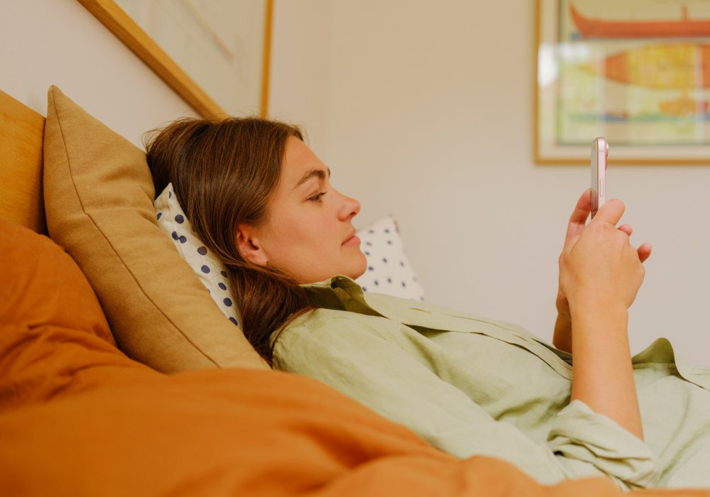 En dame som ligger i sengen, som ser på telefonen sin