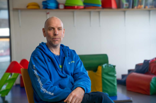 Portrett av sittende Roger Husby innendørs i blå genser.