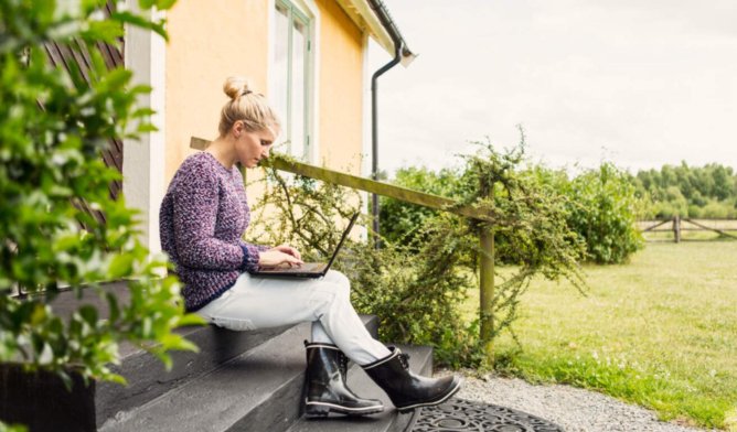 Illustasjonsfoto: Dame som sitter med laptop i fanget på en trapp utenfor huset sitt.