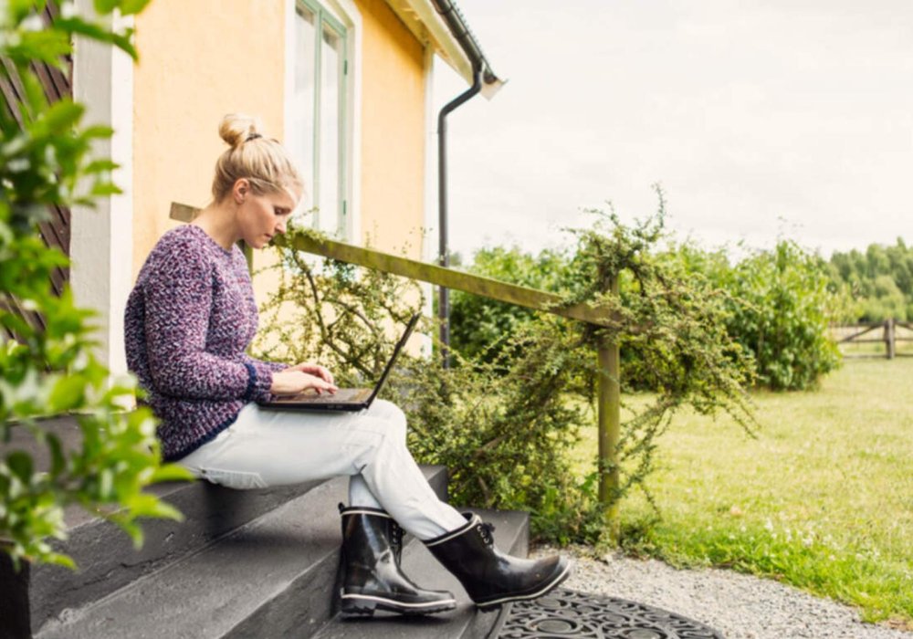 Illustasjonsfoto: Dame som sitter med laptop i fanget på en trapp utenfor huset sitt.