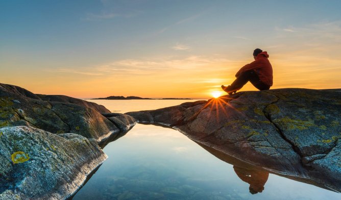 Illustrasjonsfoto: Mann som sitter på et berg i solnedgangen