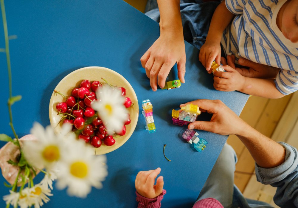 Foto ovenfra av en familie som leker med leker på stuebordet ved siden av en skål med kirsebær