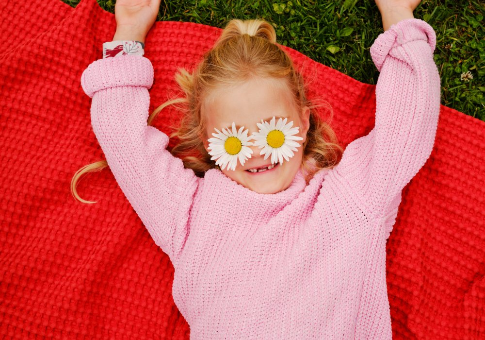 Jente som ligger på et rødt pledd med blomster foran øynene