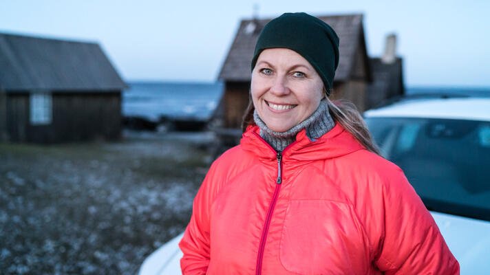 Dame i rød boblejakke foran en bil på vinterstid. 