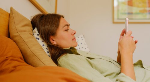 En dame som ligger i sengen, som ser på telefonen sin