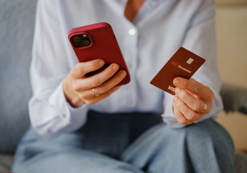 Kvinne som holder en iPhone i ene hånda, og et Storebrand-bankkort i den andre