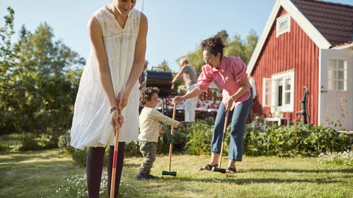 Voksne og barn som spiller krokket i hagen om sommeren.