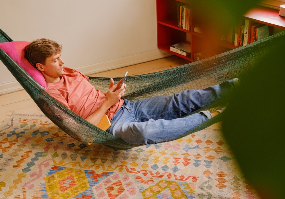 Foto av en mann som ligger i en hengekøye i stuen sin, mens han trykker på telefonen sin