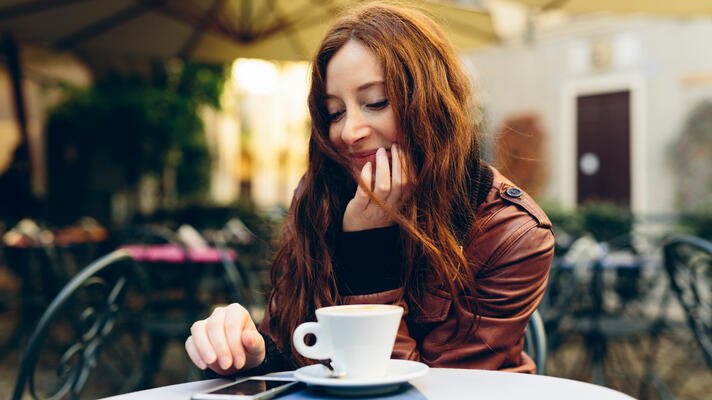 Dame på kafé som drikker kaffe og sjekker mobilen.