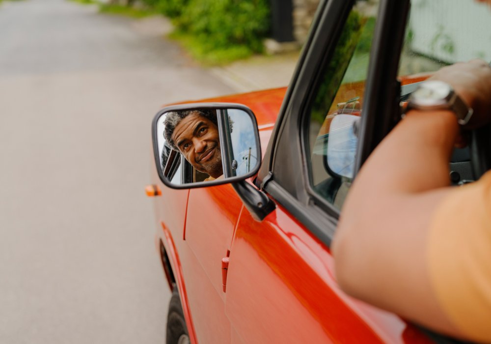 Refleksjonen av en mann i sidespeilet på en rød bil