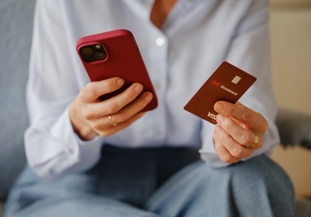 Kvinne som holder en iPhone i ene hånda, og et Storebrand-bankkort i den andre
