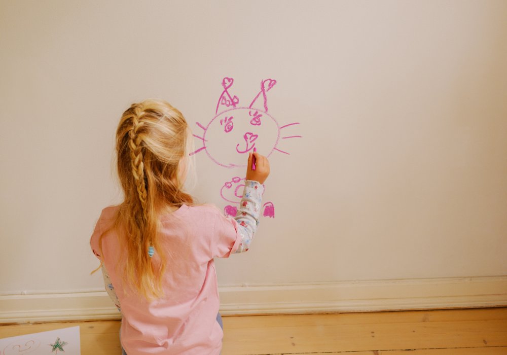 Foto av et barn som tegner på veggen med rosa fargestift
