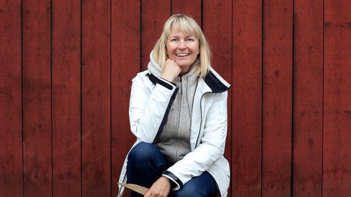 Dame som sitter ute foran en rød vegg.