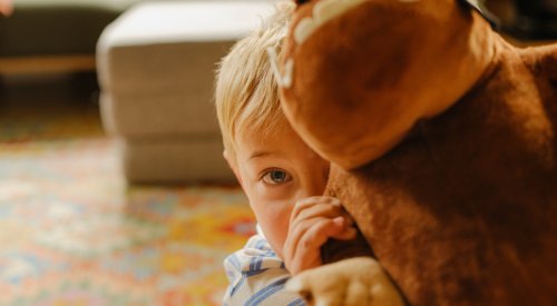 Liten gutt som gjemmer seg bak bamsen sin mens han ser inn i kamera Liten gutt som gjemmer seg bak bamsen sin mens han ser inn i kamera