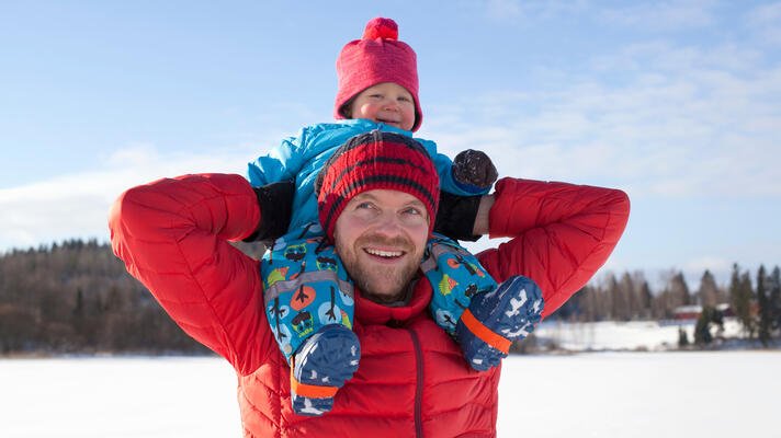 Far med baby på skuldrene, i rød jakke på vinteren.