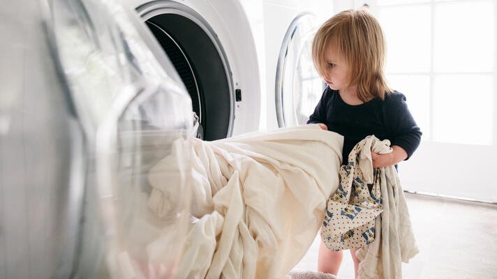 Illustrasjonsfoto: barn legger tøy i vaskemaskinen.
