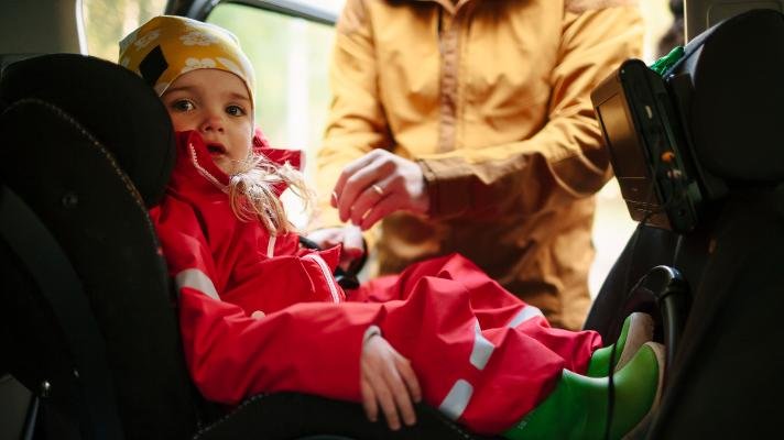 Person plasserer en liten jente i et bilsete. Foto: Johner