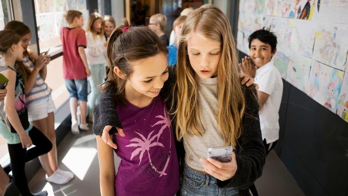 To jenter med mobil i gangen på skolen.
