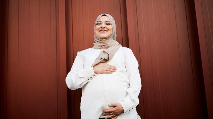 Gravid dame som står foran en rød vegg.