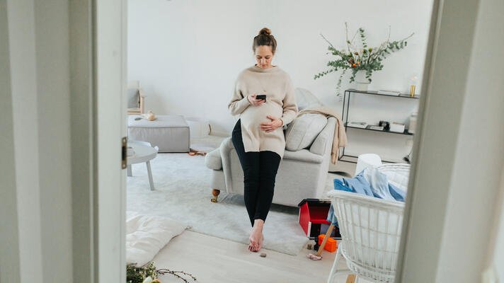 Gravid dame hjemme i stuen som scroller på mobilen sin.