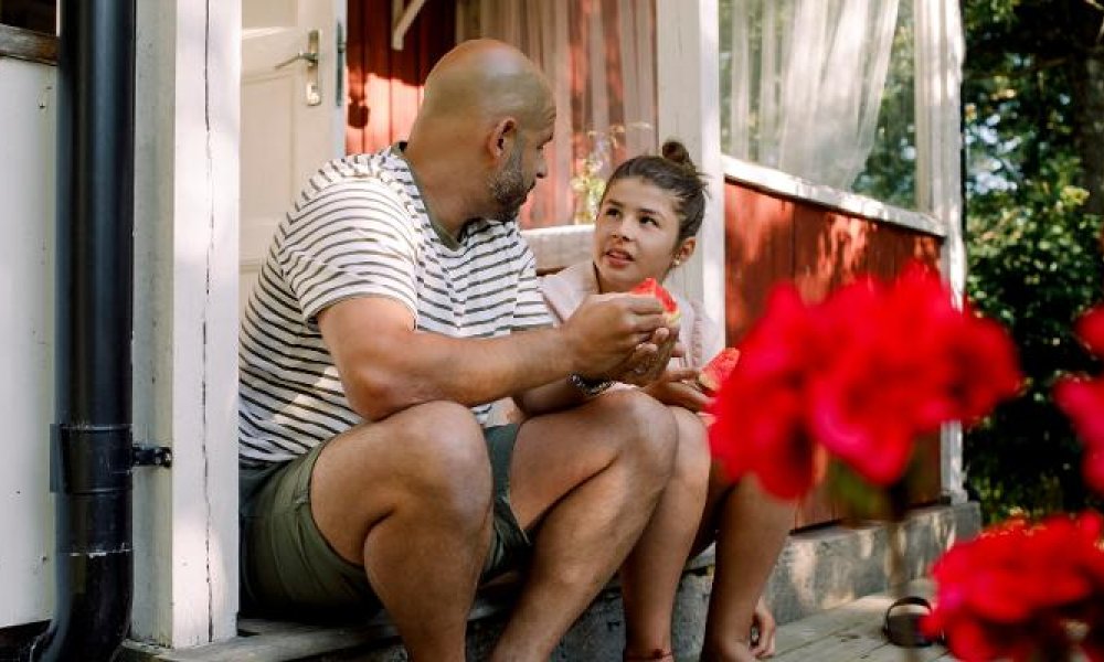 Far og datter som sitter utenfor en hytte og prater.