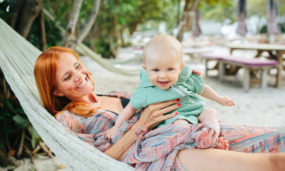 Illustrasjonsfoto: Mor med baby på fanget i en hengekøye på en sandstrand.