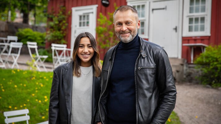 Portrettfoto av par i sorte skinnjakker, utenfor er rødt hus. 