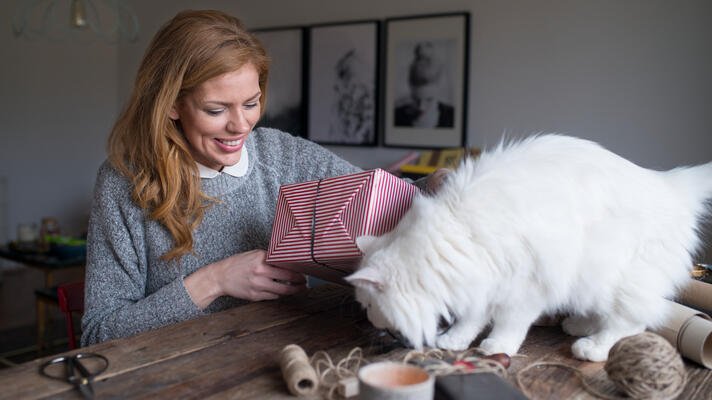 Dame som pakker inn julegaver med katten ved siden av seg.