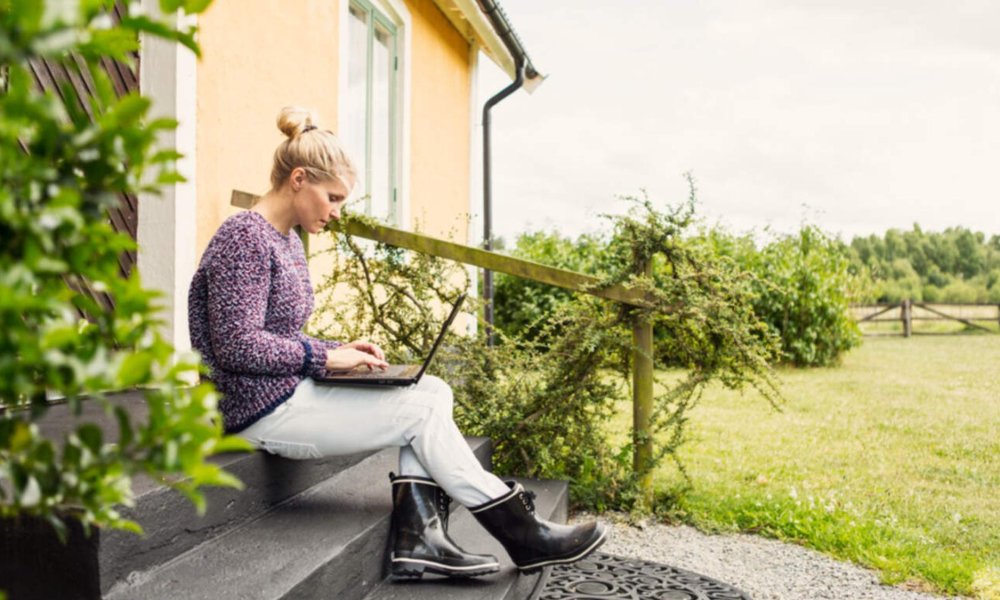 Illustasjonsfoto: Dame som sitter med laptop i fanget på en trapp utenfor huset sitt.