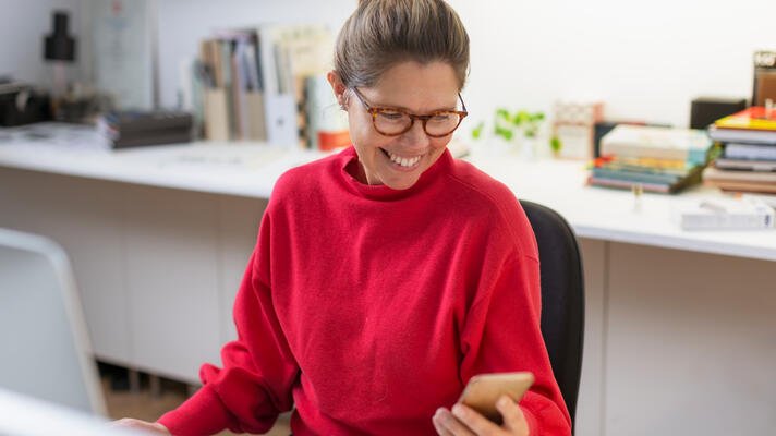 Dame i rød genser som ser på en mobiltelefon.