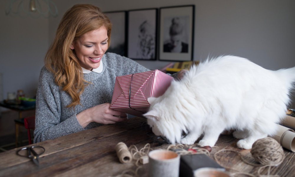 Dame som pakker inn julegaver med en katt på bordet.