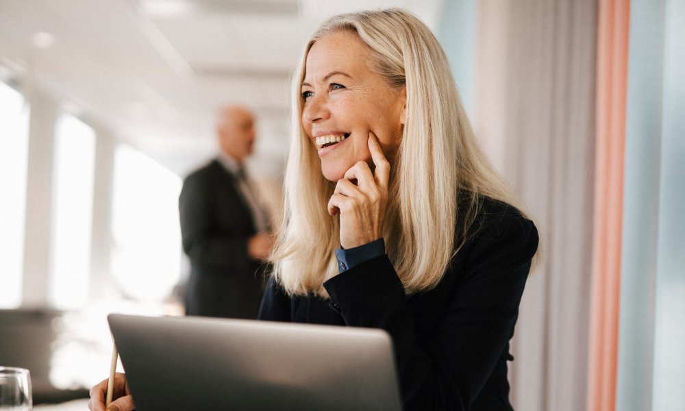 Dame sitter foran PC-skjerm på kontor og smiler. 