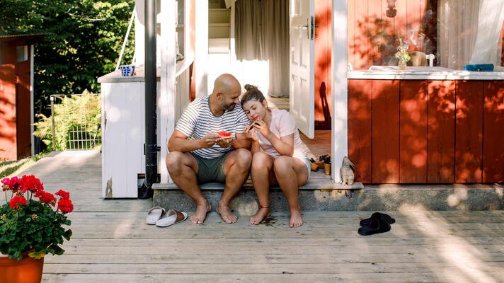 Far og datter utenfor rød hytte om sommeren.