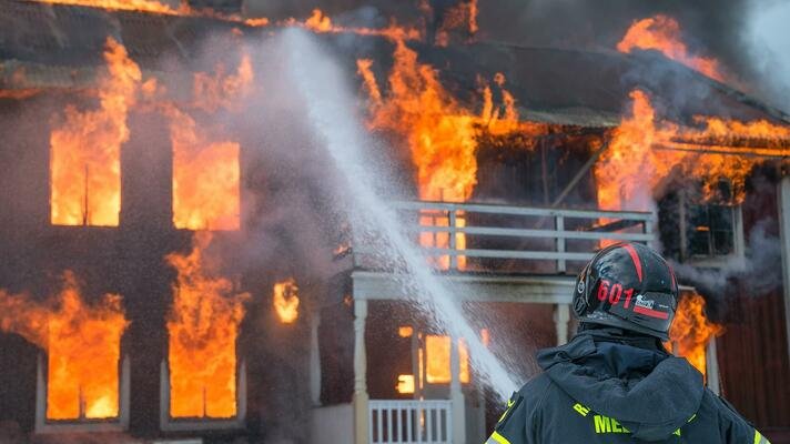 Hus som brenner og en brannmann som prøver å slukke det.