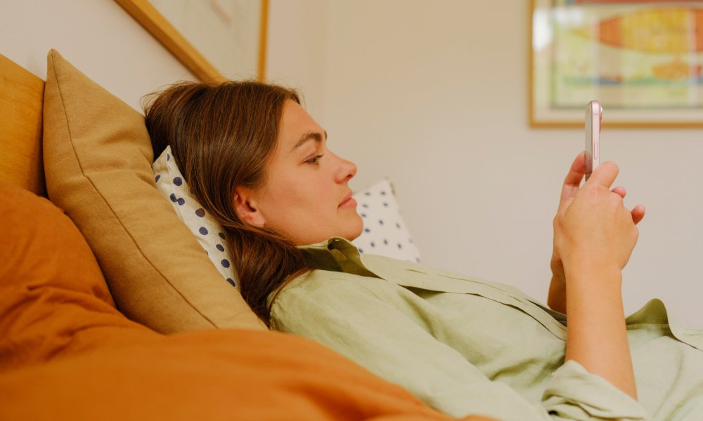 En dame som ligger i sengen, som ser på telefonen sin