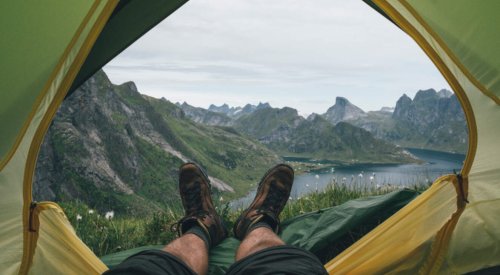 Illustrasjonsfoto: Et par bein stikker ut av et telt på fjellet med fantastisk utsikt.