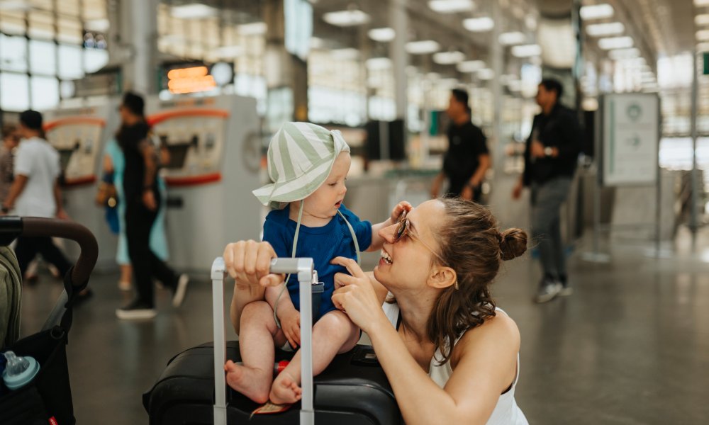 Mor med barn som sitter på en koffert på en flyplass.