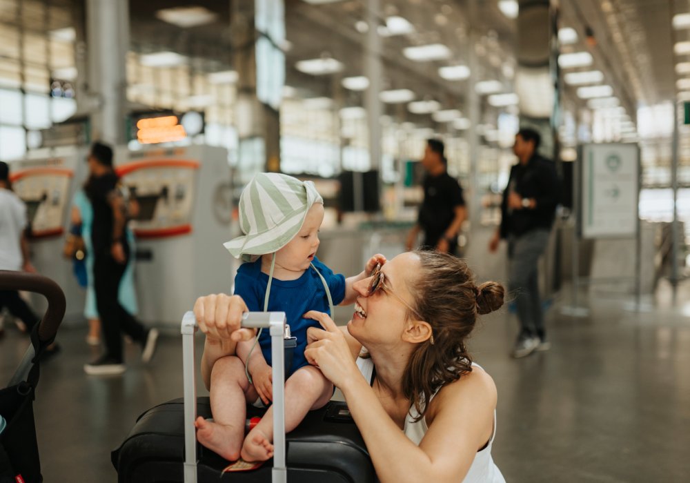 Mor med barn som sitter på en koffert på en flyplass.