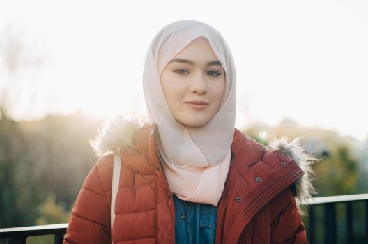 Jente i solskinn med hijab og jakke.