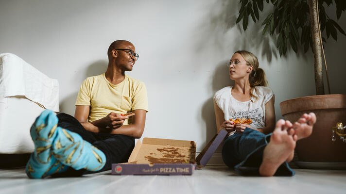 Ungt par som sitter på gulvet og spiser pizza.