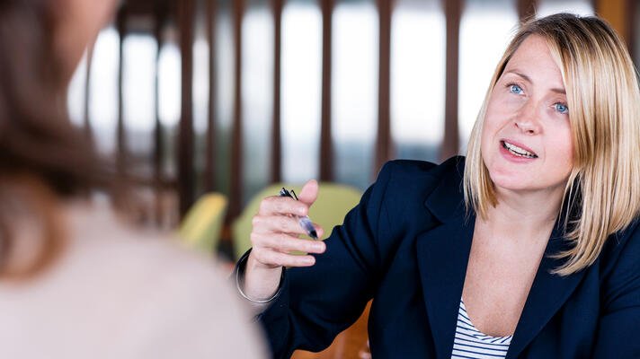 Blond dame i samtale med kollega på arbeidsplassen sin.