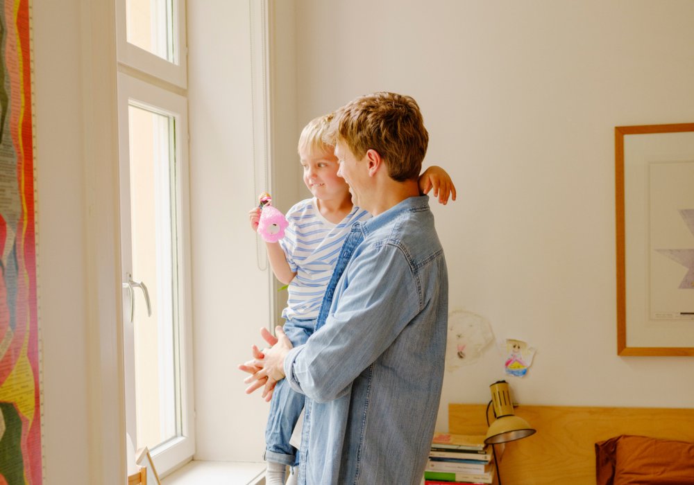 Foto av en far som holder sin sønn i armene og ser ut av et vinduet i stuen Foto av en far som holder sin sønn i armene og ser ut av et vinduet i stuen