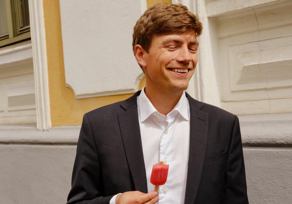 Foto av en smilende ung mann som har på seg dress og spiser lollipop på gata Foto av en smilende ung mann som har på seg dress og spiser lollipop på gata